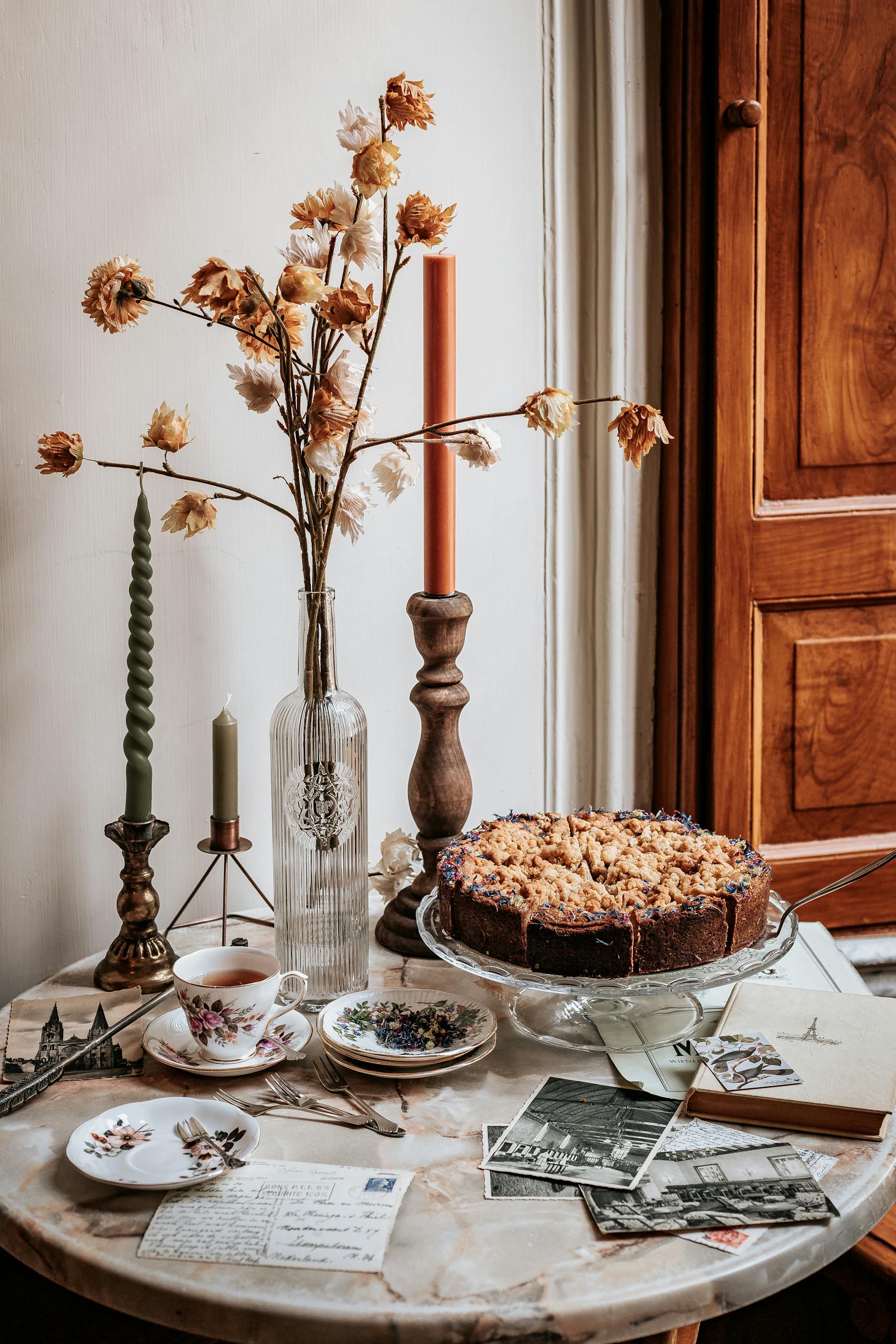 A cozy autumn still life with cake, candles, and postcards on a vintage table.