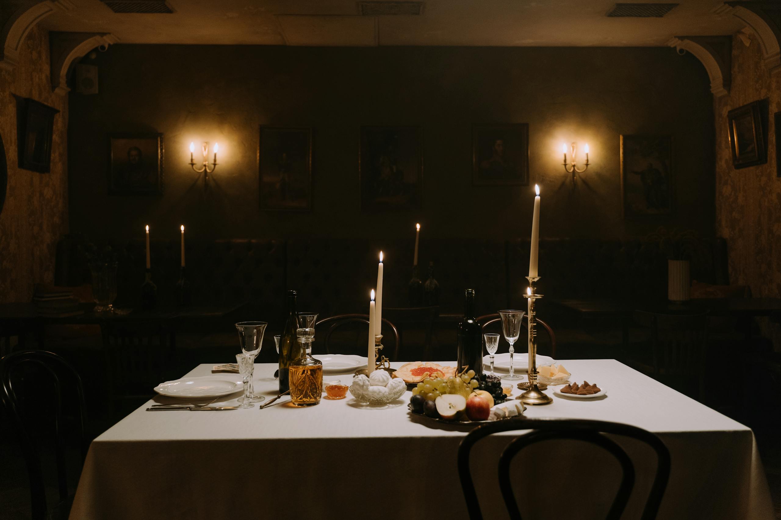 A dimly lit dining room with elegantly set table, decorated with candles, wine, and fruits for a cozy atmosphere.
