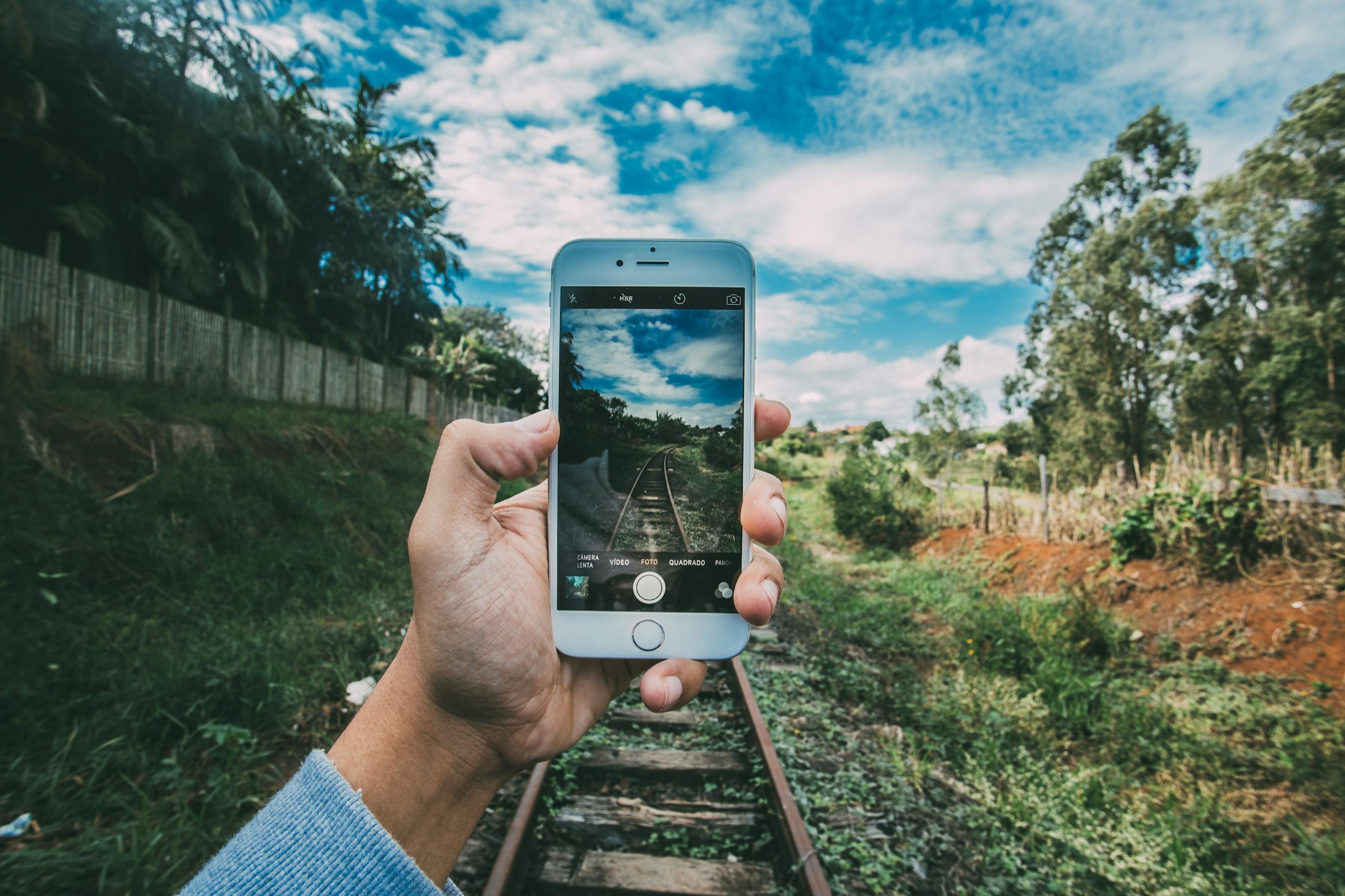 A person captures a scenic railway landscape using a smartphone outdoors.