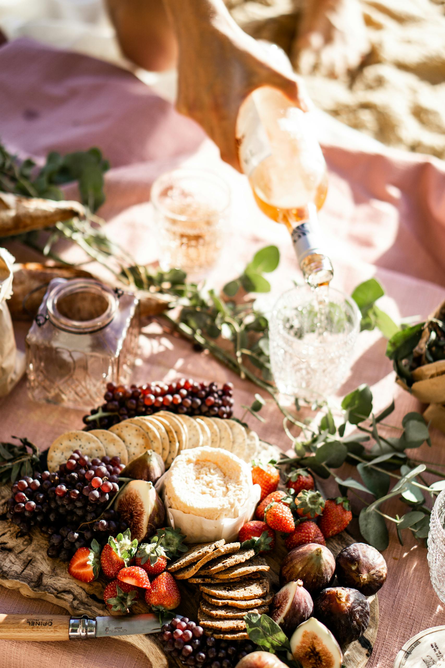 A stylish outdoor picnic with wine, cheese, figs, and strawberries on a sunny day.
