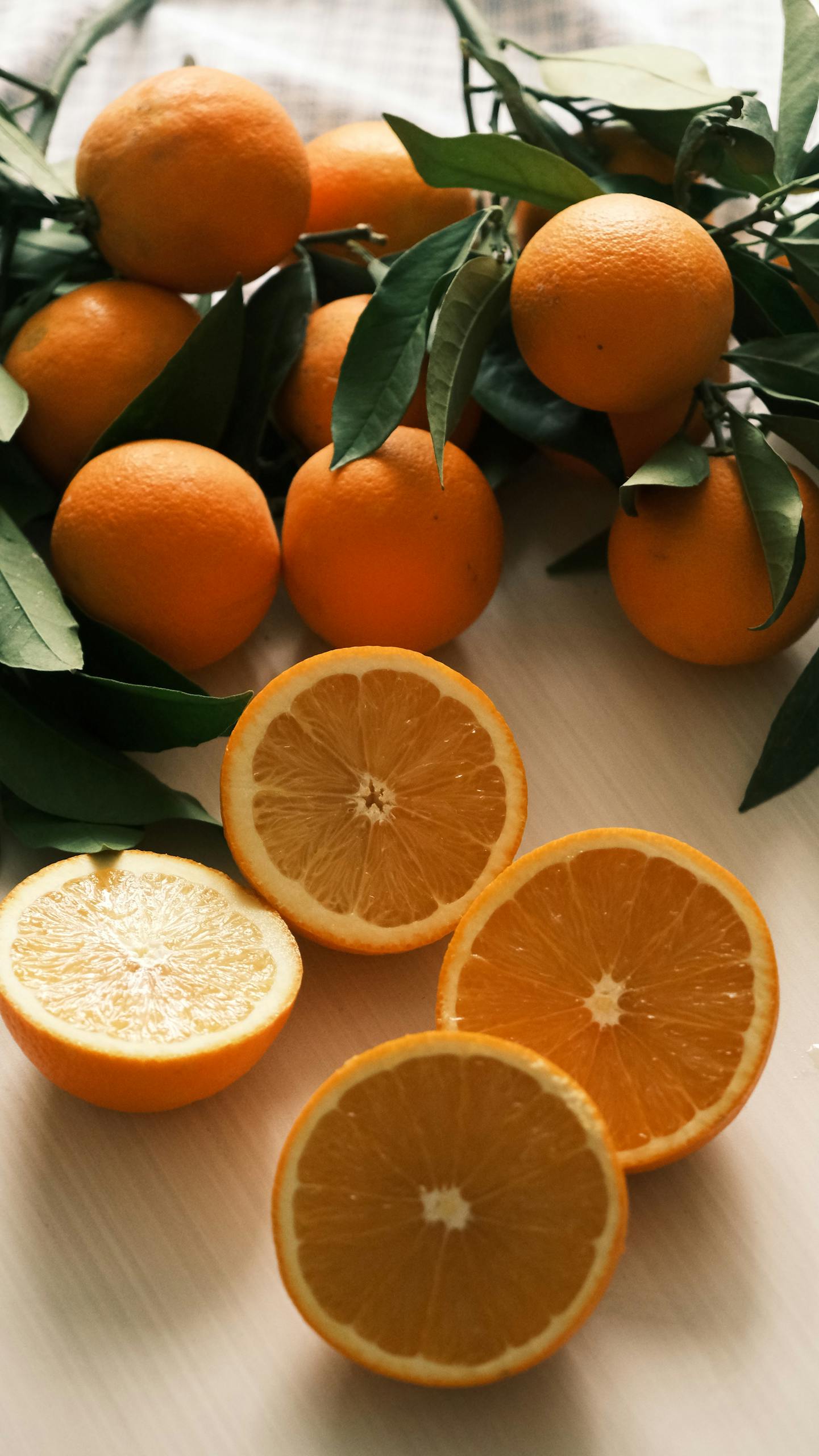 Vibrant oranges with leaves and sliced halves on a table, showcasing freshness and natural appeal.